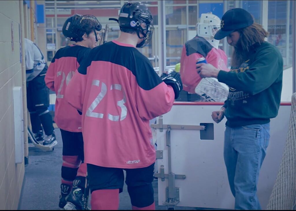 Hockey players in pink jerseys talking by the bench.