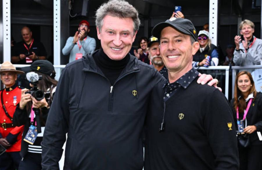 Wayne Gretzky and one other person smiling and posing together at a public event.